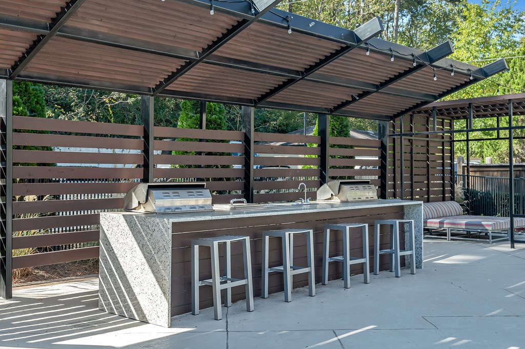 A wooden bar with a concrete counter and stools under a roof.